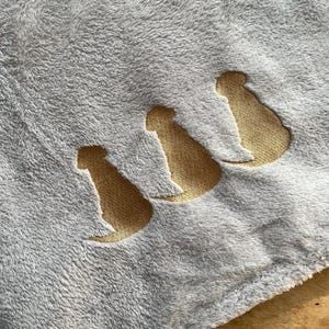 May include: A soft, gray fleece blanket with three gold embroidered dog silhouettes.