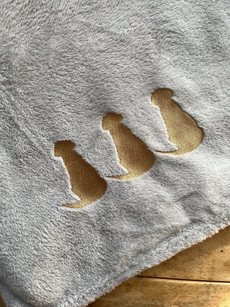 May include: A soft, gray fleece blanket with three gold embroidered dog silhouettes.