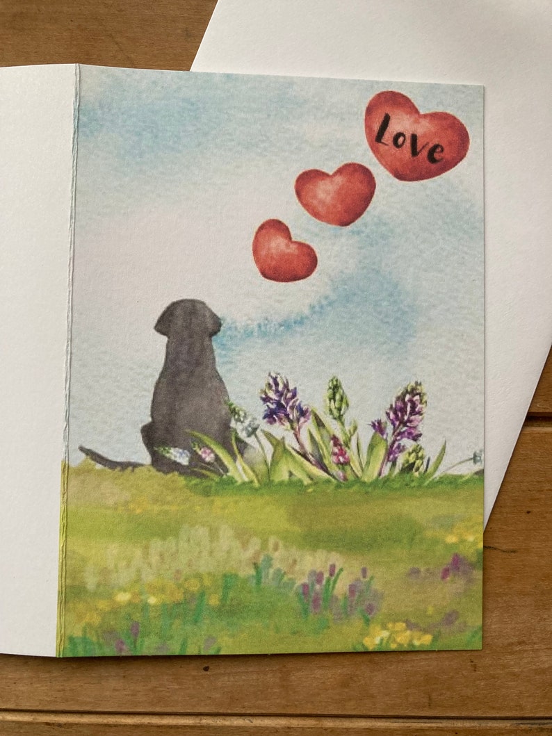 May include: A watercolor illustration of a black dog sitting in a field of purple flowers with three red hearts floating above the dog. The largest heart has the word "Love" written on it.
