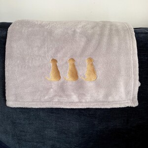 May include: A soft, gray fleece throw blanket with three gold embroidered dog silhouettes.