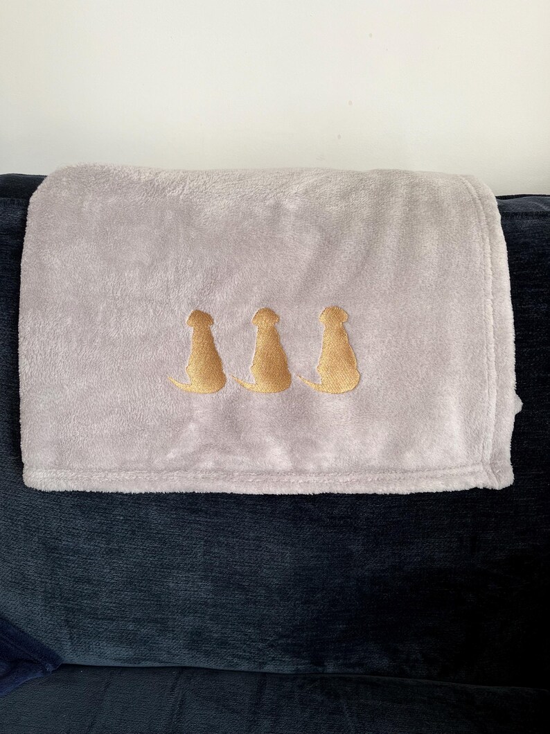 May include: A soft, gray fleece throw blanket with three gold embroidered dog silhouettes.