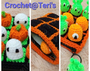 Puede incluir: Una bolsa de cremallera de crochet con temática de Halloween con un diseño en negro y naranja. La bolsa está llena de pequeñas calabazas y fantasmas de crochet. Un pequeño llavero de fantasma verde de crochet está unido al tirador de la cremallera.