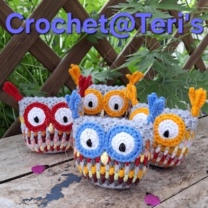 May include: Four handmade crochet owl-shaped containers in various colors. The owls have large, round eyes with white and black details, and colorful feather accents. The text "Crochet@Teri's" is visible in the image.