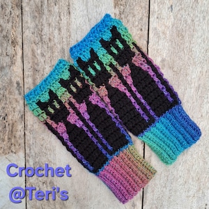 May include: A pair of handmade crochet arm warmers. The arm warmers feature a black silhouette design on a black background, with a gradient of colors including blue, green, purple, and pink. The text "Crochet @Teri's" is visible in the lower left corner.