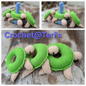 Peut inclure: Trois jouets en crochet en forme de tortues vertes avec des carapaces brunes et des yeux noirs. Les tortues sont empil&eacute;es les unes sur les autres, la tortue du bas tenant un anneau vert. Les tortues sont sur une surface en bois. Crochet@Teri's est &eacute;crit sur la surface.