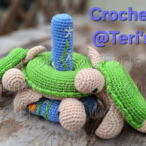 Peut inclure: Un jouet d'empilage en crochet compos&eacute; de quatre tortues vertes et beiges avec des accents bleus et blancs. Les tortues sont empil&eacute;es les unes sur les autres, la plus grande en bas et la plus petite en haut. Le jouet est fait de fil doux et est parfait pour les b&eacute;b&eacute;s et les tout-petits.