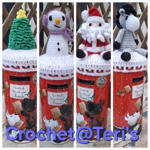 Può includere: Quattro barattoli rossi di Scottish Shortbread Rounds, ognuno sormontato da un personaggio all'uncinetto diverso: un albero di Natale, un pupazzo di neve, Babbo Natale e un cavallo. I barattoli presentano illustrazioni di cani e il testo "Scottish Shortbread Rounds". Il testo "Crochet@Teri's" è anche visibile.