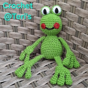 May include: A handmade green crochet frog with white and black eyes, red cheeks, and a smiling mouth. The frog has long arms and legs with webbed feet. The text "Crochet @Teri's" is in the upper left corner.