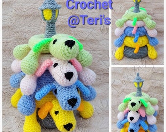 May include: A crocheted stackable toy featuring four colorful dogs with a gray lamppost on top. The dogs are green, pink, blue, and yellow. The toy is a great educational tool for children.