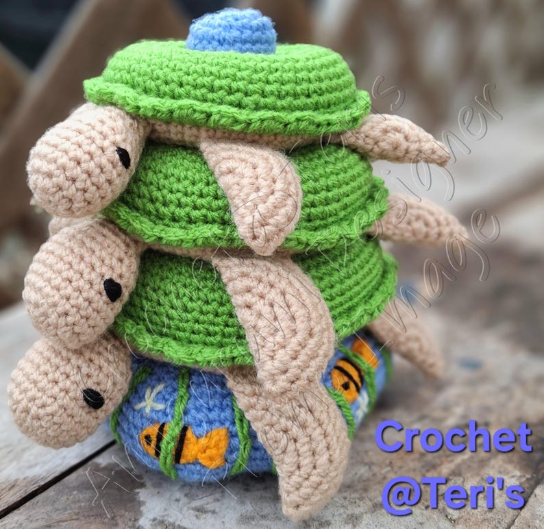 Peut inclure: Une pile de quatre tortues de mer en crochet. La tortue du bas est bleue avec des poissons orange et des algues vertes. Les trois tortues du haut sont vertes avec des t&ecirc;tes et des pattes beiges. Crochet @Teri's.