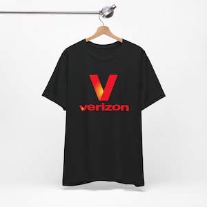 May include: Black t-shirt featuring a red and yellow "V" logo and the word "verizon" in red. The t-shirt is displayed on a wooden hanger.