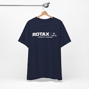 May include: Navy blue t-shirt with the white text "ROTAX AIRCRAFT ENGINES" and the Can-Am logo. The t-shirt is hanging on a wooden hanger against a white background.