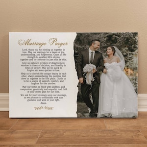 May include: A canvas print featuring a wedding photo and a "Marriage Prayer" in elegant script. The photo shows a smiling couple, the bride in a white gown, the groom in a suit. The print is on a wooden surface.