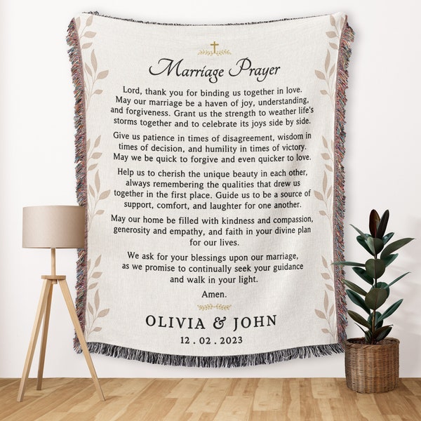 May include: Cream-coloured woven throw blanket with a Marriage Prayer printed in black. The blanket features a decorative border with floral accents and fringe. The names Olivia & John and the date 12.02.2023 are printed at the bottom.