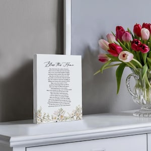 Puede incluir: Un letrero de madera blanco con un dise&ntilde;o floral y el texto "Bless This Home". El letrero tiene un poema sobre el hogar y la familia.