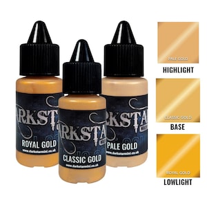 Puede incluir: Tres botes de pintura dorada Darkstar Miniatures: Royal Gold, Classic Gold y Pale Gold. Cada bote tiene una tapa negra y una etiqueta con el nombre de la marca y el sitio web. También se muestran muestras de color para resaltado, base y sombra.