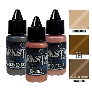 Puede incluir: Tres botes de pinturas metálicas Darkstar Miniatures: Blackened Bronze, Bronze y Antique Gold. Cada bote tiene una tapa negra y una etiqueta con el nombre de la marca y el color. También se muestran muestras de color para Highlight, Base y Lowlight.