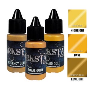 Puede incluir: Tres botes de pintura acrílica dorada metálica con tapas negras. Las botellas están etiquetadas como "Regency Gold", "Royal Gold" y "Braid Gold". También se muestran muestras de color para "Highlight", "Base" y "Lowlight". El sitio web www.darkstarmini.co.uk está impreso.