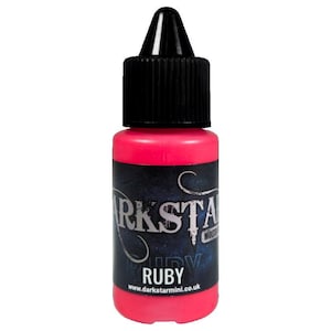 Może przedstawiać: Mała, żywa, różowa butelka farby w płynie "Ruby". Butelka ma czarną zakrętkę i etykietę z nazwą marki "Darkstar" oraz adresem strony internetowej. Farba przeznaczona jest do malowania miniatur.