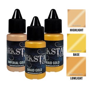 Puede incluir: Tres pequeños frascos de pintura metálica con tapas negras. Las botellas están etiquetadas como "Imperial Gold", "Braid Gold" y "Raid Gold". Las muestras de color muestran "Fine Gold", "Braid Gold" e "Imperial Gold". El texto "Darkstar Miniatures" es visible.