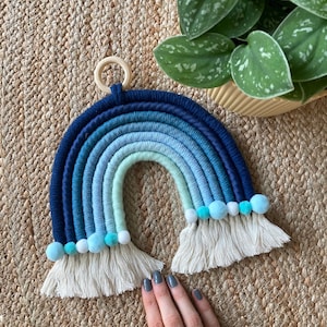 May include: A blue and green ombre rainbow wall hanging with white tassels and blue pom poms. The rainbow is made of yarn and has a wooden ring at the top.