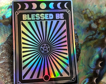 May include: A black and silver holographic sticker with a pentagram, moon phases, and the text "Blessed Be".