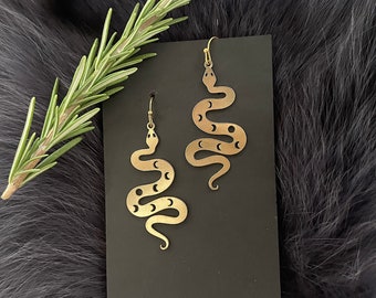 May include: A pair of gold-toned snake earrings with a crescent moon design. The earrings are hanging from a black card.