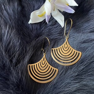 May include: A pair of gold-toned earrings with a geometric fan-shaped design. The earrings have a simple hook closure.