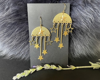 May include: Gold tone earrings with a half-moon shape and dangling stars. The earrings are displayed on a black card.