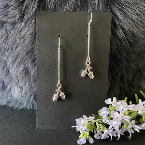 May include: A pair of silver dangle earrings with acorn charms. The earrings are hanging from a black card.