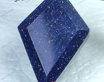 May include: A dark blue gemstone with a faceted, diamond-shaped cut. The gemstone is covered in tiny, iridescent sparkles.