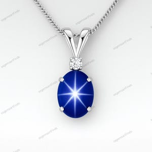 May include: A silver pendant necklace featuring an oval, deep blue gemstone with a star-like pattern. The pendant is accented with a small, round diamond and hangs from a delicate chain. The jewelry is set against a white background.