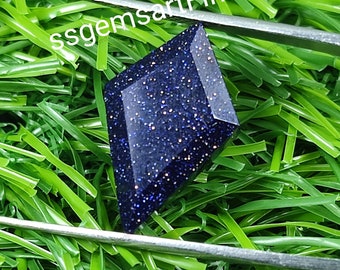 May include: A dark blue gemstone with a sparkly, glittery finish. The gemstone is cut in a kite shape and is set against a green background.