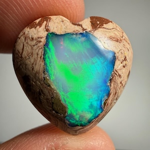 Puede incluir: Una piedra preciosa pulida en forma de corazón con una incrustación central de ópalo azul y verde vibrante. La piedra circundante es una matriz de color canela y marrón con un patrón orgánico jaspeado. La pieza tiene una superficie lisa y redondeada.