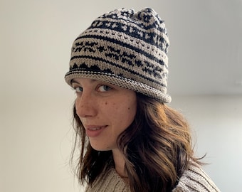 Könnte beinhalten: Eine Person trägt eine schwarze und beige Strickmütze mit geometrischem Muster. Die Mütze hat einen schwarzen Rand und ist umgeklappt.