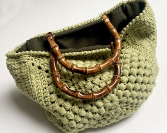 May include: A light green crocheted tote bag with brown bamboo handles. The bag has a green fabric lining.
