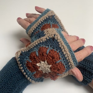 May include: A pair of handmade crochet fingerless gloves. The gloves feature a square design with a floral pattern in shades of teal, rust, and beige. The cuffs are a solid teal color, and the gloves are displayed against a white background.