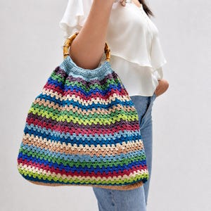 Può includere: Una borsa tote all'uncinetto fatta a mano, multicolore, con manico in bambù. La borsa presenta un vivace motivo a righe nei toni del blu, verde, rosso e beige. La borsa è di grandi dimensioni, perfetta per trasportare l'essenziale quotidiano.
