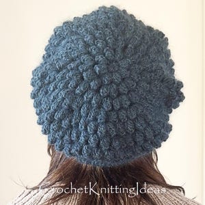 Op de afbeelding: Een donkerblauwe gehaakte hoed met een getextureerd oppervlak. De hoed heeft een nauwgebreid patroon en een licht opstaande rand. De tekst "crochetKnittingIdeas" is zichtbaar onderaan de afbeelding.