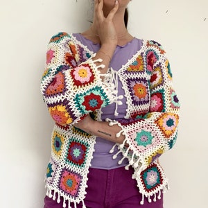 May include: A white crochet cardigan with colourful granny squares and fringe trim. The cardigan has a tie closure at the front.