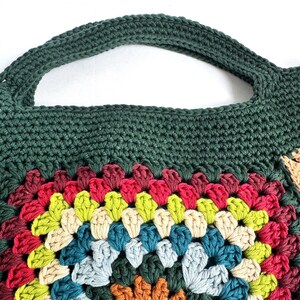 Puede incluir: Bolso tote de crochet hecho a mano con asa y parte superior verde oscuro. El bolso presenta un dise&ntilde;o de granny square colorido con tonos de rojo, amarillo, azul y crema. El bolso est&aacute; hecho de hilo suave, ideal para llevar objetos cotidianos.