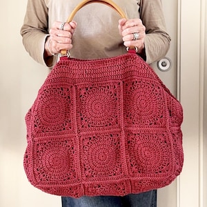 May include: A large, red crocheted tote bag with a wooden handle. The bag is made of square panels with a circular pattern.
