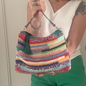 May include: A colorful crocheted handbag with a green tassel. The bag has a brown leather strap and is made with a variety of different colored yarns.