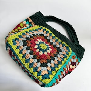 Puede incluir: Bolso tote de crochet hecho a mano con un patr&oacute;n geom&eacute;trico colorido. El bolso presenta un asa y ribete verde oscuro, con un dise&ntilde;o de patchwork vibrante en tonos de rojo, verde, azul y beige. Un accesorio elegante.