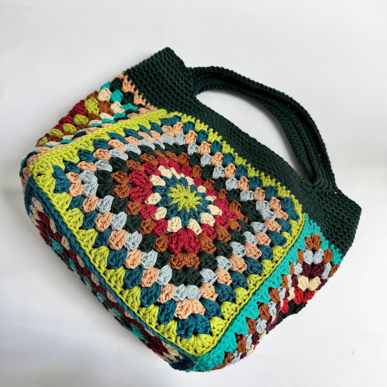 Puede incluir: Bolso tote de crochet hecho a mano con un patr&oacute;n geom&eacute;trico colorido. El bolso presenta un asa y ribete verde oscuro, con un dise&ntilde;o de patchwork vibrante en tonos de rojo, verde, azul y beige. Un accesorio elegante.