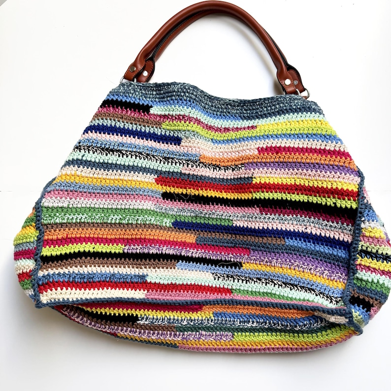 May include: A large, colorful crochet bag with a patchwork design. The bag features a variety of colors, including red, blue, yellow, and green. It has brown leather handles and a spacious interior, perfect for carrying essentials.