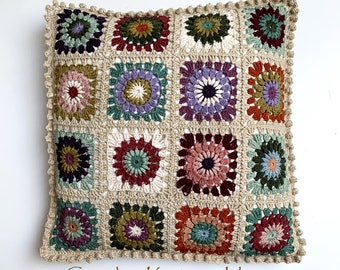 May include: A crocheted pillow with a square pattern of colorful flowers. The pillow is beige with a brown border and has a crocheted fringe.