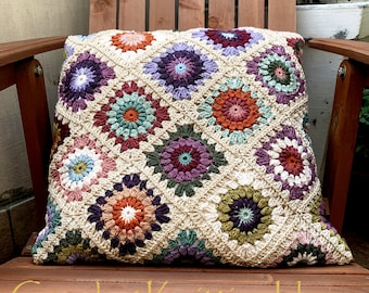 May include: A crocheted pillow with a geometric pattern of colorful flowers. The pillow is made with a variety of shades of brown, green, purple, and pink.