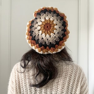May include: A crocheted beanie in a multi-colored pattern of brown, black, white, and beige. The beanie is worn on a person's head.