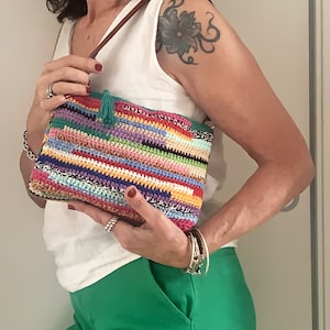May include: A colorful crocheted crossbody bag with a green tassel. The bag is made with a variety of different colored yarns, including red, orange, yellow, green, blue, purple, and white.